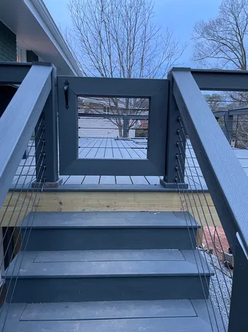 Dark composite deck stairs with cable railing and swinging gate installed at a residential home