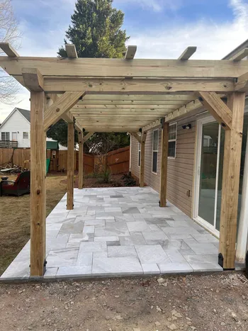 Open wood pergola over a newly completed travertine tile patio adjacent to a residential home