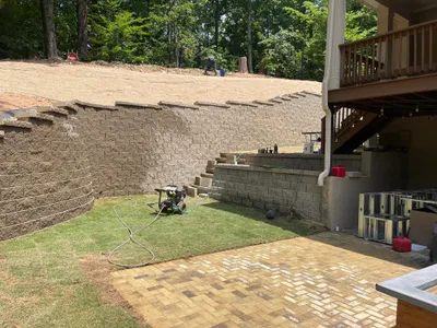 Large segmental block retaining wall installation beneath a residential deck with paver patio below