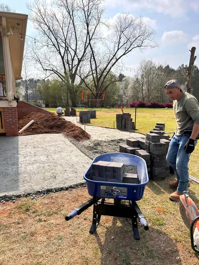 Crew member laying pavers to build a patio base beside a craftsman-style brick home