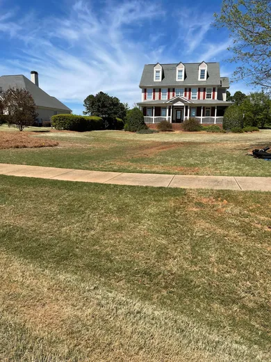 Image of a freshly trimmed yard with a colonial style home in the background. 